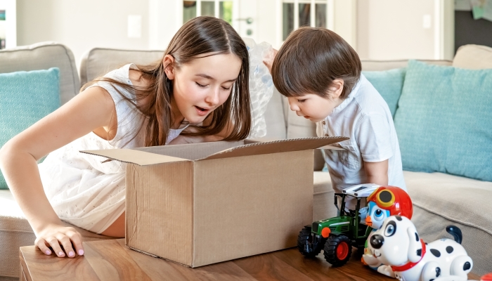 Happy children unpacking box with toys delivered by courier to house.