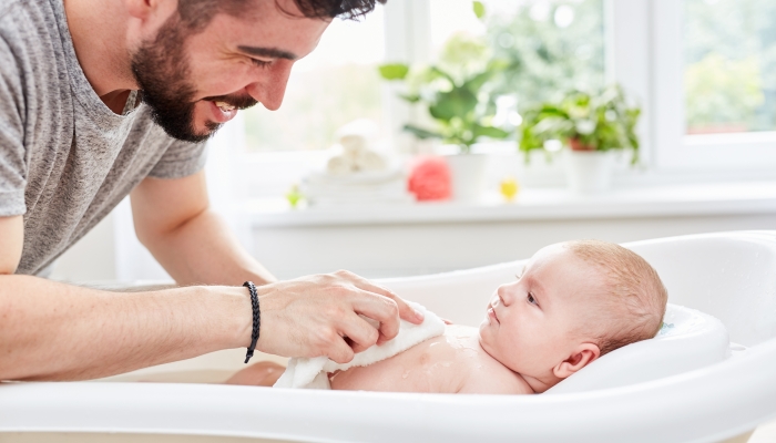 Happy father washes his baby caring with the washcloth.