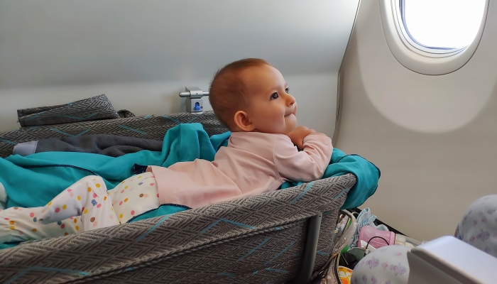 Happy infant baby lyes in special bassinet in airplane at his stomach.
