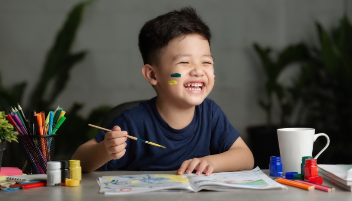 Happy little kid at the table draw with water color.