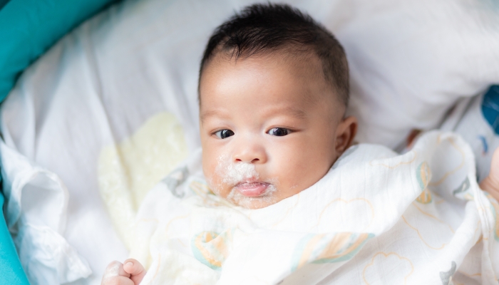 Infant baby boy vomit after eat milk on bed.