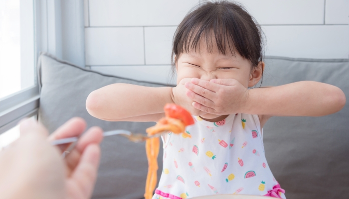 Little asian girl close her mouth by hands,refuse to eat tomato in spagethi from her mother.