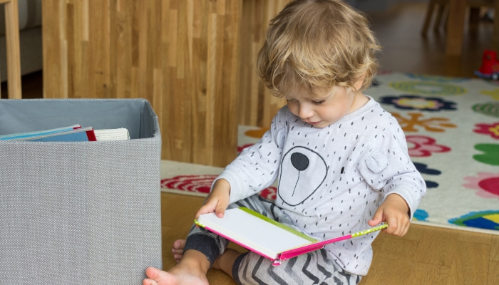 Little boy sitting with a book on the floor.