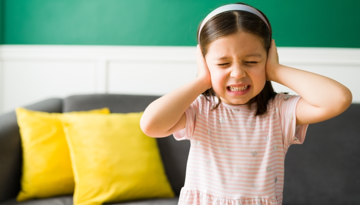 Little girl covering her ears because of screaming and loud sounds at home.