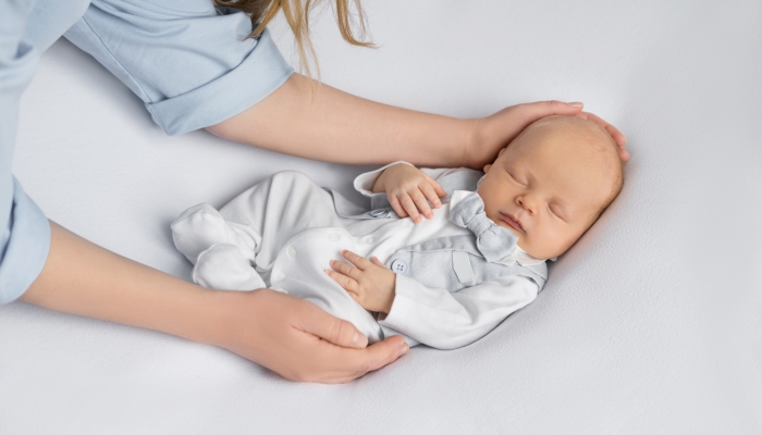 Mom's hands hold newborn baby boy in a suit sleeping.