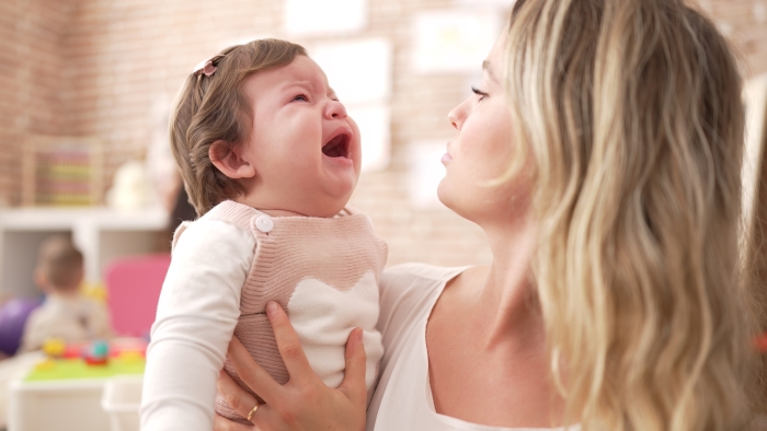 Mother and daughter consueling baby crying at kindergarten.