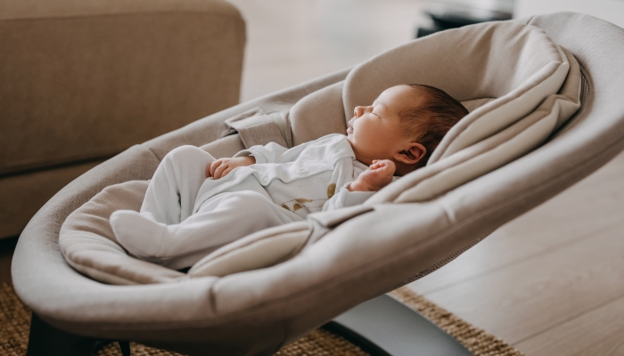 Newborn baby sleeping in a swing, wearing a white onesie pajama.