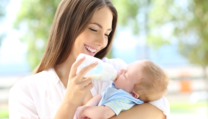 Portrait of a happy mother giving bottle feeding to her baby outdoors.