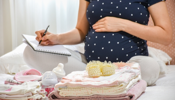 Pregnant woman is packing baby clothes for going to maternity hospital.