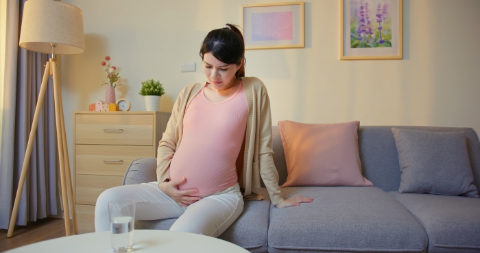 Pregnant woman is suffering abdominal pain sitting on sofa in the living room.