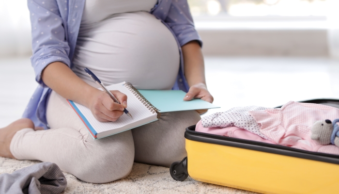 Pregnant woman writing packing list for maternity hospital at home.