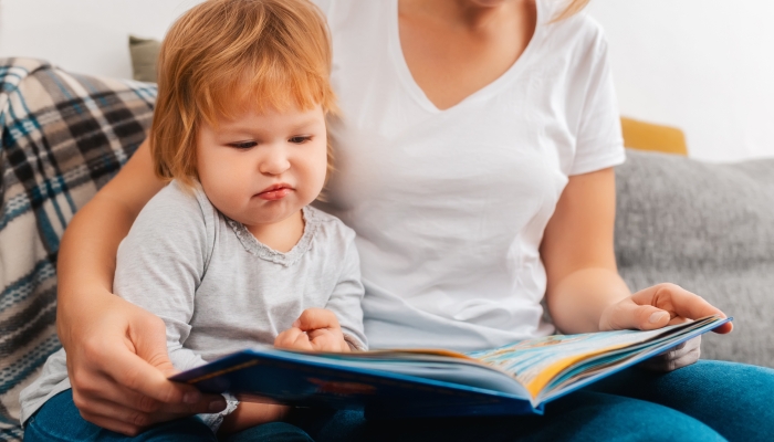 Speech therapist is reading a book to bored child sitting on the sofa.