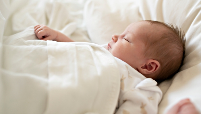 Sweet newborn baby girl sleeping in white bed.