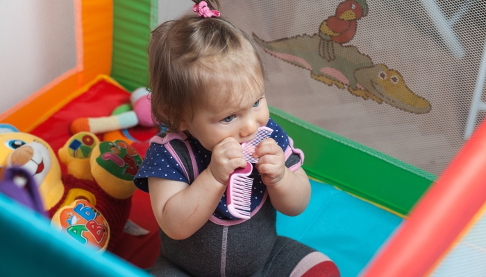 Teething caucasian blonde baby girl playing with a plastic comb.