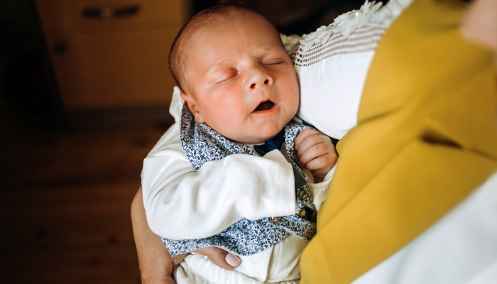 The baby sleeps in the arms of the mother.