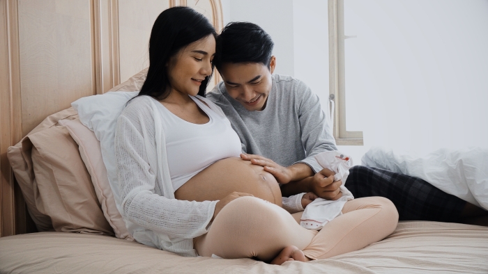 Young father holding a baby clothes and talking with pregnant wife.