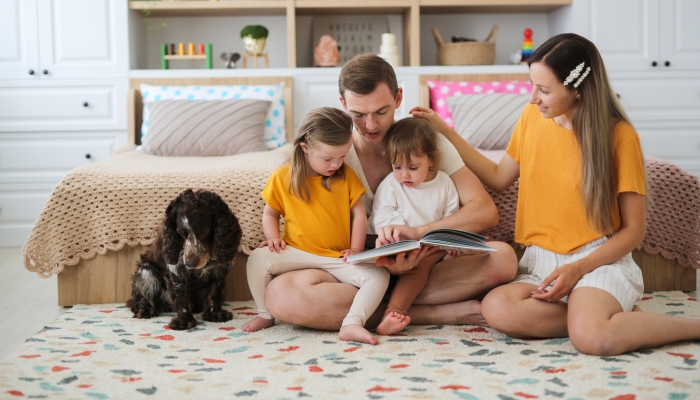 a beautiful family with two children and a dog reading a book together.