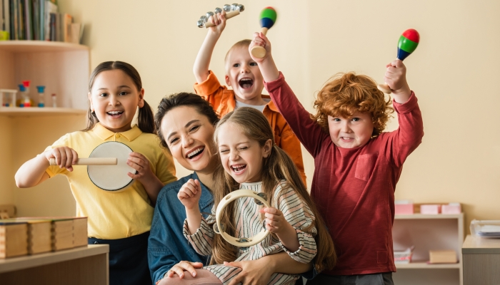 Excited multiethnic kids playing musical instruments near happy teacher.