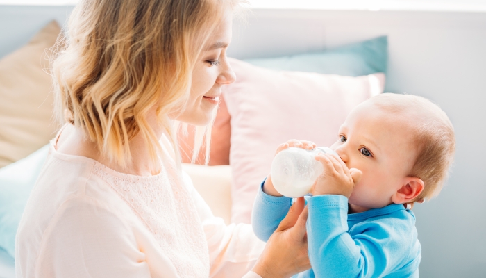 happy mother feeding her little child with baby bottle at home.