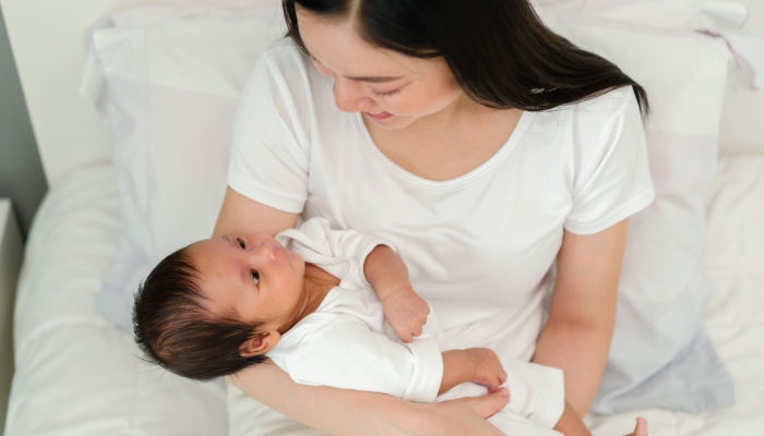 mother holding and talking with her newborn baby on a bed.