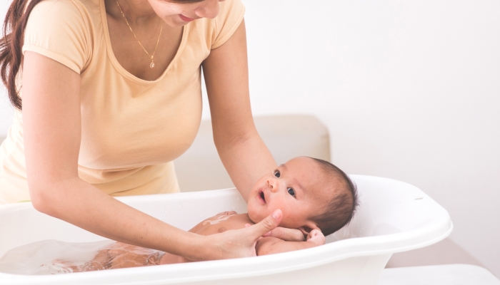 portrait of a baby is being bathed by his mother using tub at home.