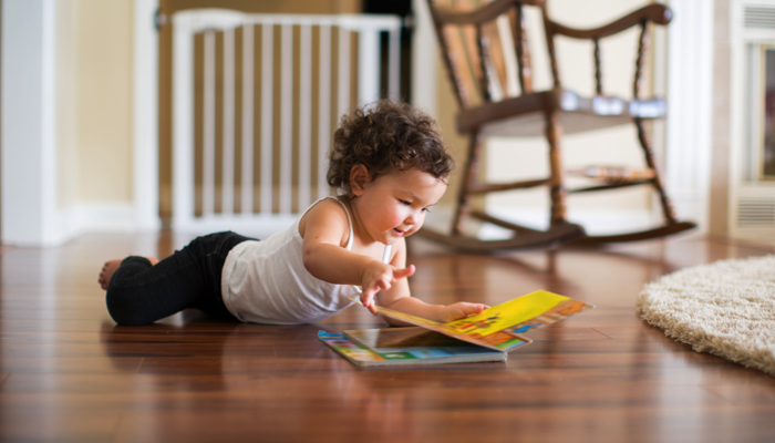 Toddler on the floor reading a board book.