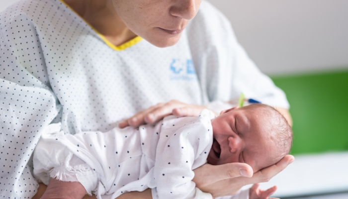 young mother who has just had her baby in the hospital holds the newborn in her arms gently patting him on the back to help him pass gas after feeding.