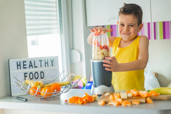 A cute little boy in a yellow T-shirt makes himself a fruit smoothie in the kitchen.