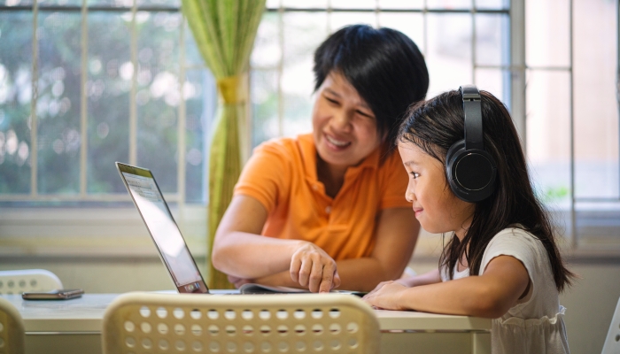 Asian girl and her teacher using laptop for online study during homeschooling at home.