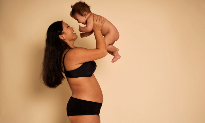 Asian woman in underwear holding a toddler above head.