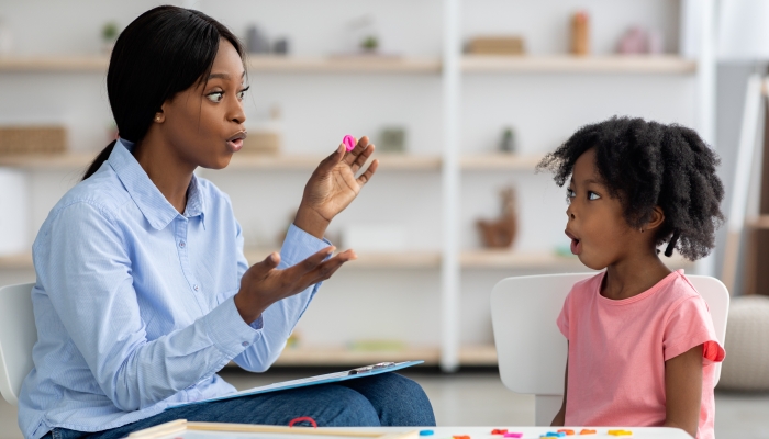 Attractive young african american woman speech therapist working with little black girl.