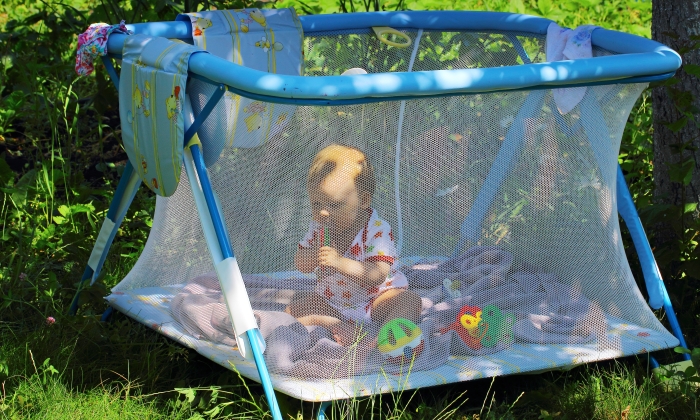 Baby sitting in the playpen in the shade garden trees and likes to play with toys.