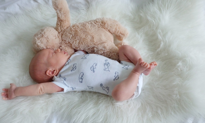 Baby sleeping on white fur with stuffed animal.