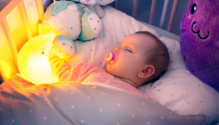 Baby sleeps in bed with lighting moon and soft toys in the night.