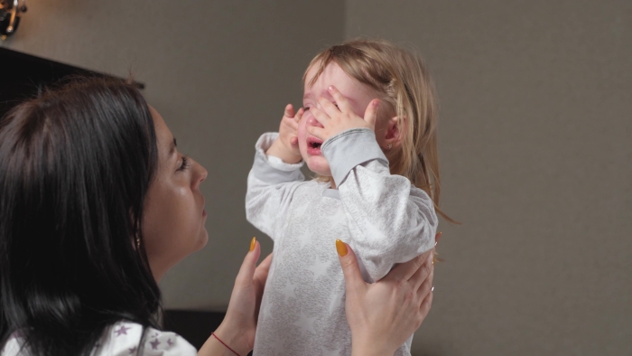 Child is crying in room in the arms of his mother.