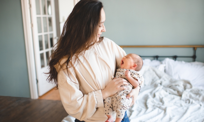 Crying baby girl on mother hands with colic stomach ache in bed.