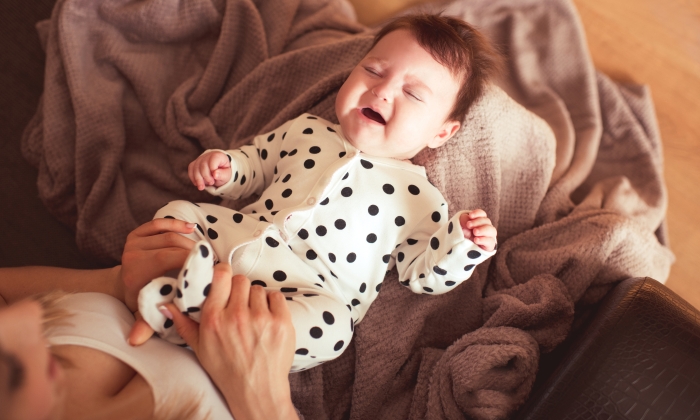 Crying baby on mother hands in room.