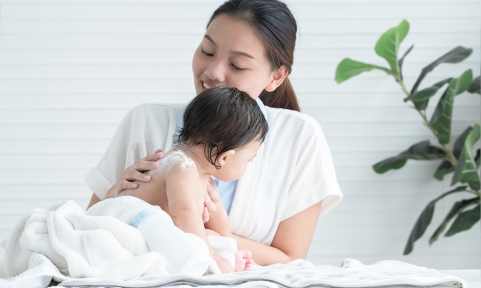 Cute Caucasian little naked toddler baby girl sitting on towel after bathing and wipe body dry while young.