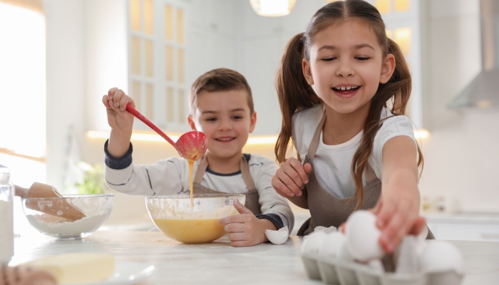 Cute little children cooking dough together in kitchen.