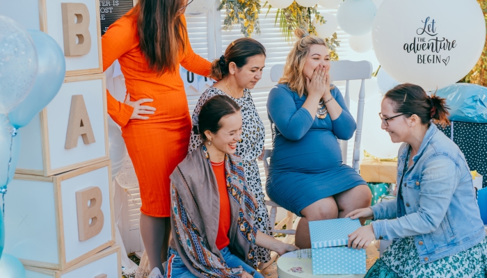 Female friends open gift boxes with a pregnant woman at a baby shower.