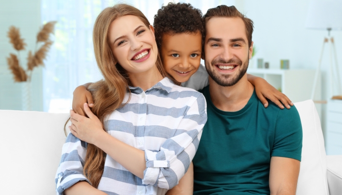Happy couple with adopted African-American boy sitting on couch at home.