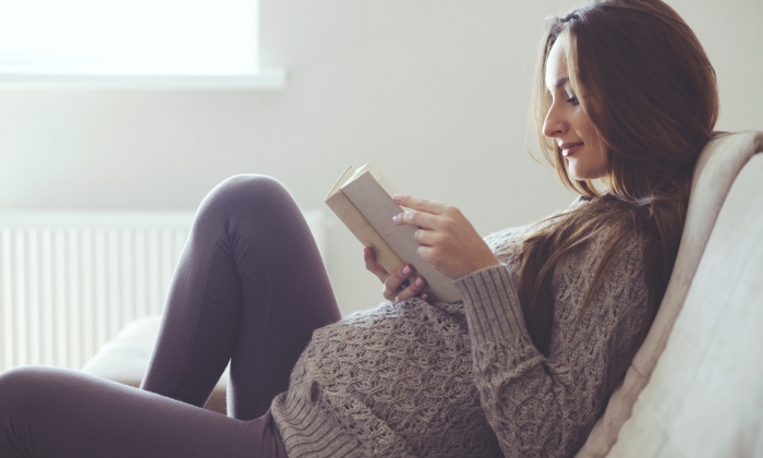 Home cozy portrait of pregnant woman resting at home and reading book on sofa.