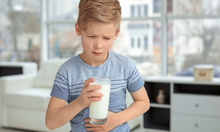 Little boy with dairy allergy holding glass of milk indoors.