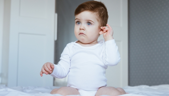 Little boy with ear pain moaning holding hand on ear at home.