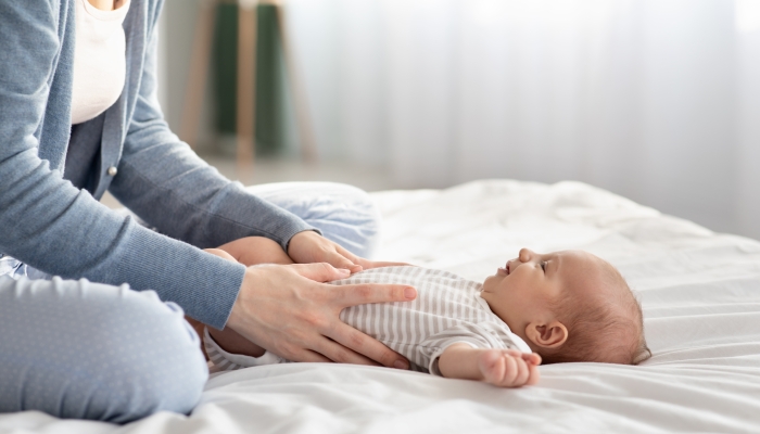 Loving Mother Making Belly Massage To Her Newborn Baby On Bed At Home.