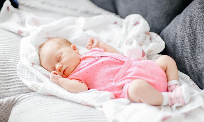 Newborn baby girl sleep on white blanket and wearing pink clothes.