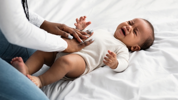 Portrait of black mother doing belly massage for crying baby.