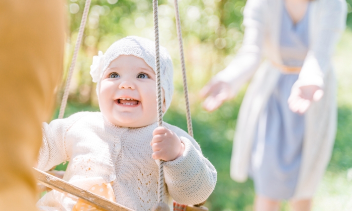 Stylish young parents swings their happy one-year-old daughter, on a wooden swing.