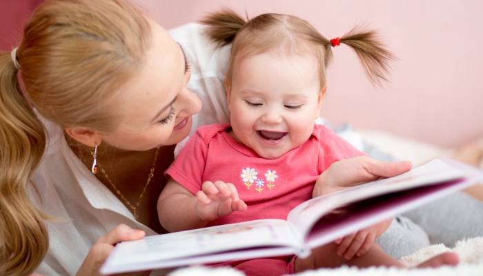 Happy mother read a book to child girl indoors.