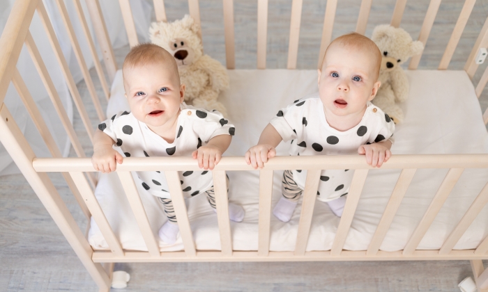 Two baby twins brother and sister 8 months sit in their pajamas in the crib.